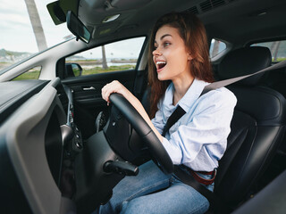 A woman is in the driver's seat of a car with her hands on the steering wheel, mouth wide open,...