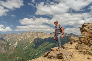 Fototapeta premium A man looks at the high snow-capped mountains. The conquest of the mountains. The rocks are located high in the mountains. The nature of the highlands.