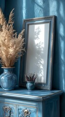 Photo of a vertical picture frame with blank white paper leaning against the wall on top of an elegant sideboard, in light blue and gray tones. The background is a clean blue wall with some pampas