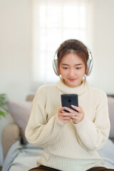 Young asian women in sweater wearing headphone and surfing entertainment with listening music on smartphone while relaxation and doing activity for spending time with slow life lifestyle at home