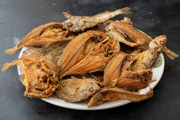 Ikan masin goreng or fried salted fish in white plate, isolated on black background. Malaysian and Indonesian traditional food.