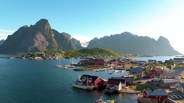 An aerial view of the stunning Lofoten Islands in Norway shows vibrant cabins that contrast beautifully with majestic mountains, creating an enchanting landscape to explore