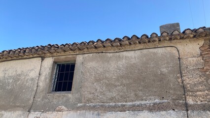 Detalle de ventana rota en casa de pueblo abandonada, vacía. Cielo azul.