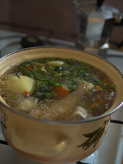 Chicken Soup Simmering in a Yellow Pot with Moka Coffee Machine in the Background – Vertical Close-Up