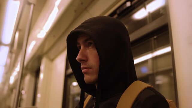 Close-up of unfriendly suspicious black hooded young man look around in a moving subway car 4K