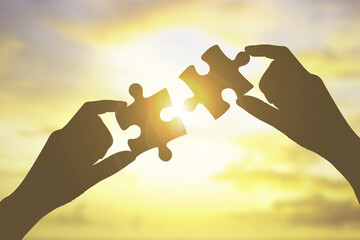 hand with two jigsaw puzzle on sunset sky blur background