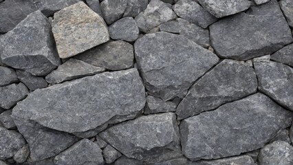 Fototapeta premium Close-up of a dry stone wall with irregularly shaped gray stones tightly stacked together. The image showcases the rough texture and natural patterns of the stones, ideal for backgrounds