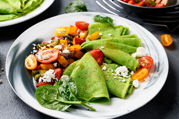 Fresh prepared delicious green spinach crepes served with colorful baked peppers and cherry tomatoes. 