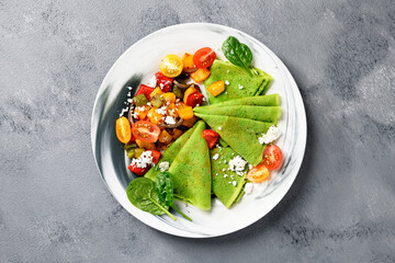 Fresh prepared delicious green spinach crepes served with colorful baked peppers and cherry tomatoes. top view