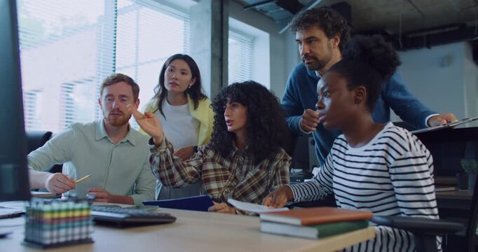 Group of multi-ethnic colleagues gathering together in front of one monitor. Woman in middle with curly hair confused about something. People pointing at screen. Team meeting. Finding solution.