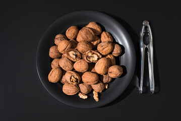 Nueces y cascanueces en un plato negro sobre fondo negro. Vista superior	