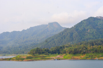 A tranquil landscape with a lake among the clouds. A mountain river flows from forested hills to a glacial lake. Snowy mountains in the mist. A small river and coniferous trees are reflected in a calm