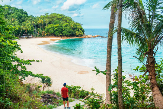 Man tourist stand on stone steps over tropical sandy beach with turquoise water ocean. Male traveler walking down to Freedom beach in Phuket island, Thailand with nobody. Summer vacation in Asia