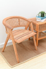 Wooden chair and side table with a plant, books, and basket in a cozy setting.