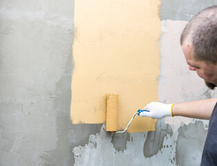 A hand in a white glove paints a light yellow wall with a roller, moving from left to right
