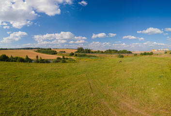 Landscape view from drone, yellow and green fields and haystacks, sky with white clouds. 