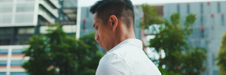 Young businessman is walking down the street and looking at a smartphone on modern building background, panorama