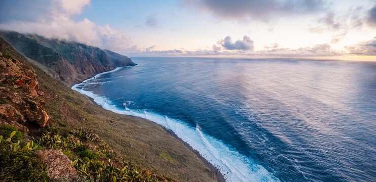 View of rough ocean with waves, volcanic beach, sunset over a huge cliff  in Lighthouse Ponta do Pargo, Madeira, Portugal