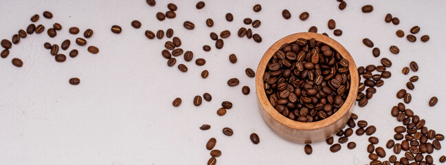 Freshly roasted coffee beans spilled from a wooden bowl on a neutral background