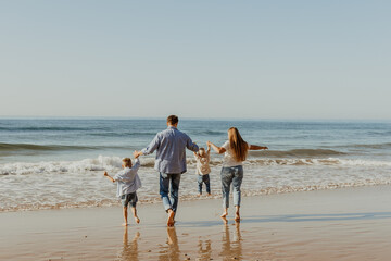 Happy family of four people with small kids walking and having fun near the ocean on the sunny...