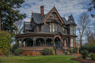 Fototapeta premium Mystical Victorian mansion with intricate gothic details and lush greenery, evoking a hauntingly beautiful aura amidst a tranquil blue sky.