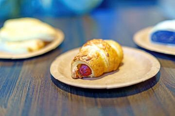 golden-brown croissant wraps a savory sausage, resting on a simple paper plate. This delightful...