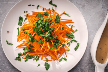 Carrots and parsley, finely thinly sliced on a white plate on a gray background with a fork on a green napkin. Dietary Nutrition Concept