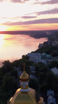 Aerial view of the sunset sky above the wide river. Clip. Green town located along the river.