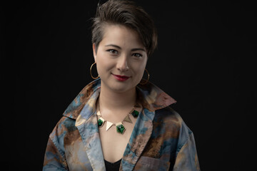 The image showcases a woman with a vibrant smile, dressed in a multi-colored shirt, accessorized with hoop earrings and a geometric necklace, against a dark background.