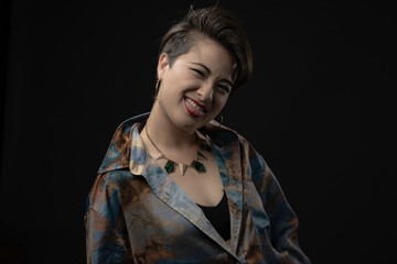 A young woman wearing artistic clothing with bold colors, winks playfully to the camera, expressing happiness. Showcased on a dark background to highlight her features.
