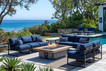 Blue outdoor seating group with armchairs, sofas, and a central fire pit, surrounded by a pool and garden, featuring dark navy cushions, a wooden table, and clear skies with sunlight.