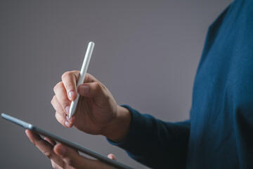 A person using a stylus to write or draw on a digital tablet, highlighting modern technology in...