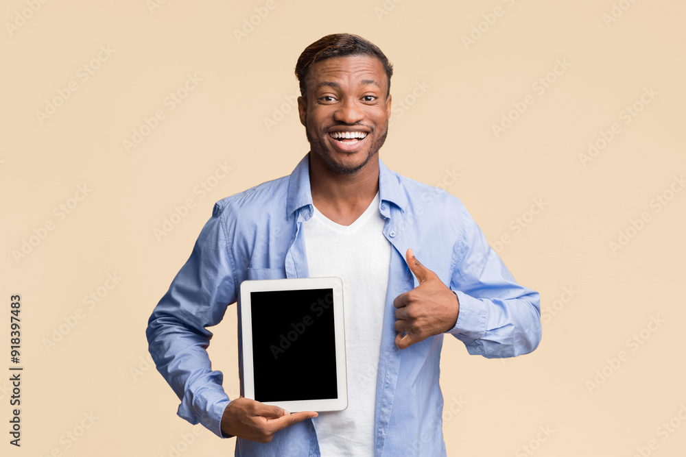 Poster cheerful afro man showing empty tablet screen gesturing thumbs up smiling at camera standing over ye
