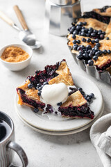 A piece of homemade blueberry pie served with a scoop of ice cream and mint on light gray table background