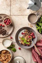 Granola with yogurt, chocolate, fresh raspberries and mint on beige tile background. Organic food for healthy and dieting breakfast, top view