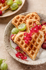Homemade waffles with summer berries and yogurt served for sweet breakfast on beige background close up. Heart shaped waffles