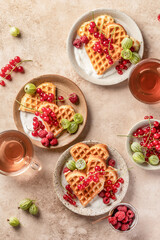 Homemade waffles with summer berries and yogurt served for sweet breakfast with tea on beige background. Heart shaped waffles top view