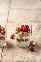 Berry dessert in glass with granola, fresh raspberries, yogurt or cream cheese. Healthy breakfasr concept, on beige tile background with text space