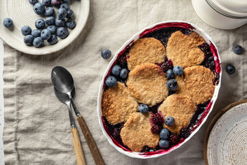 Homemade blueberry cobbler pie in baking dish on linen tablecloth table top view, flatly, sweet breakfast