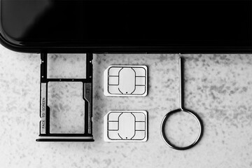 smartphone and open slots for micro SD and nano SIM cards, two nano SIM cards and metal key on grey background top view black white photo