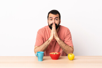 Caucasian man having breakfast in a table keeps palm together. Person asks for something.