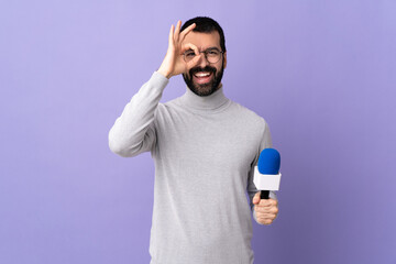 Adult reporter man with beard holding a microphone over isolated purple background showing ok sign...