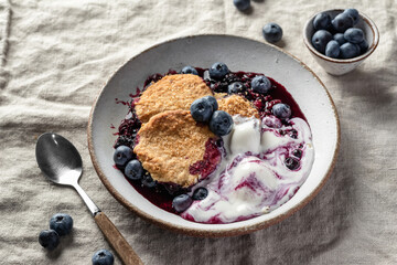 Homemade blueberry cobbler pie served with scoop of ice cream in ceramic plate on linen tablecloth table, sweet breakfast