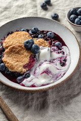 Homemade blueberry cobbler pie served with scoop of ice cream in ceramic plate on linen tablecloth table close up, sweet breakfast