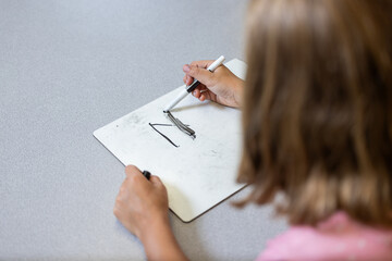 A girl is writing on a white board. She is using a black marker. Concept of focus and concentration...