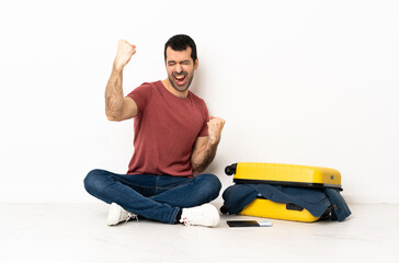 Caucasian handsome man with a suitcase full of clothes sitting on the floor at indoors celebrating a victory