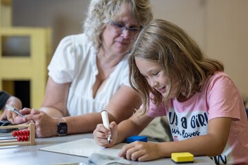 A teacher is helping a child with a math problem. The teacher is reviewing the students work in the classroom setting.