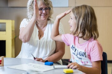 A teacher is helping a young girl with her math homework. The girl is wearing a pink shirt and is...