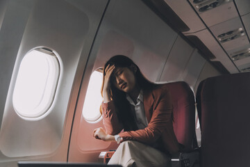 Photo of a frustrated woman sitting on an airplane with her head in her hands. Asian woman sitting...