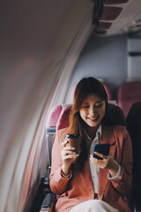 Attractive Asian female passenger of airplane sitting in comfortable seat while working laptop and tablet with mock up area using wireless connection. Travel in style, work with grace.